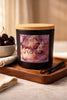 Matte black jar candle with light wood lid and purple floral label reading 'Phoenix Crafted Black Cherry Vanilla'.