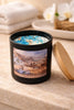 Matte black cylindrical candle labeled 'Coastal Orchid Woods' with white wax topped by blue crystals and a short wooden wick.