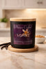 Matte black jar candle with light wood lid on wood coaster, purple label Phoenix Crafted - Vanilla, vanilla pods at left.