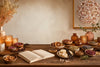 Artisan fragrance storytelling scene with candles, wax melts, dried citrus, rose petals, vanilla, herbs, spices, and a blank notebook.