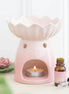 Pale-pink water-lily wax warmer with scalloped bowl, tealight in front opening, and amber dropper bottle with pink label and loose black dropper.