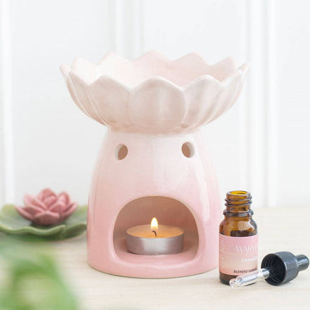 Pale-pink water-lily wax warmer with scalloped bowl, tealight in front opening, and amber dropper bottle with pink label and loose black dropper.