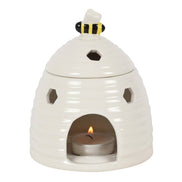 White ceramic beehive-shaped tealight warmer with hexagonal cutouts, bee figurine lid knob with black-and-yellow stripes.
