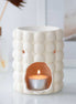 Cream speckled bubble-textured ceramic tealight wax warmer with open front cavity holding a lit aluminum tealight.