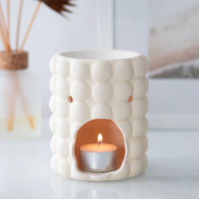 Cream speckled bubble-textured ceramic tealight wax warmer with open front cavity holding a lit aluminum tealight.