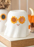 White ceramic ghost wax warmer wearing orange flower-shaped sunglasses and a small painted smile on a tabletop