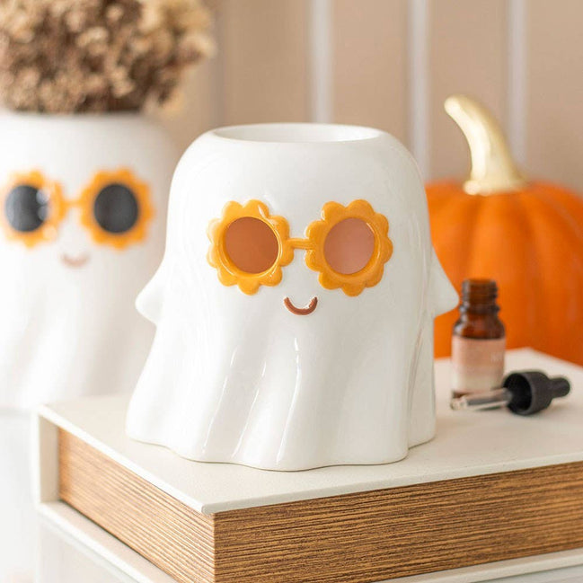 White ceramic ghost wax warmer wearing orange flower-shaped sunglasses and a small painted smile on a tabletop