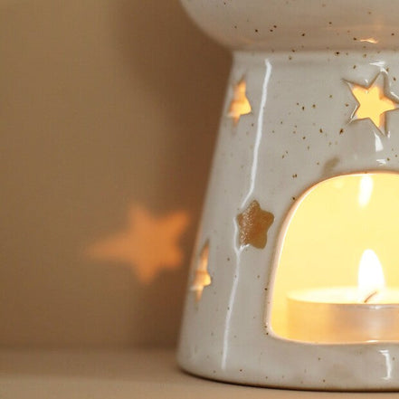 Starry wax melt ceramic warmer with star-shaped cut-outs and soft glaze, glowing with tealight candle light.