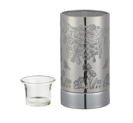 Silver cylindrical metal wax warmer with laser-cut honeybee, hexagon and floral pattern; clear glass cup positioned left