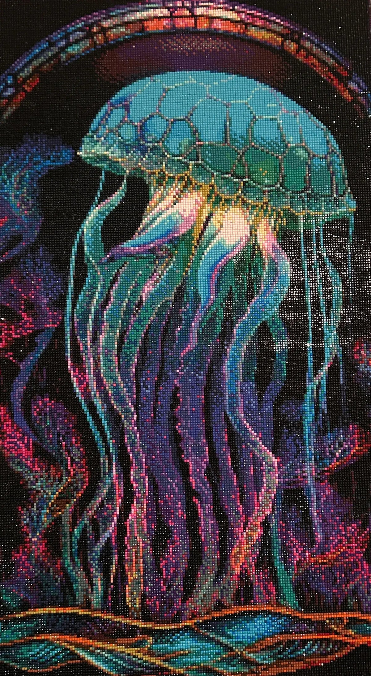 Close-up diamond painting of a teal jellyfish with hexagon-patterned bell and flowing blue, purple and pink tentacles on a black background.