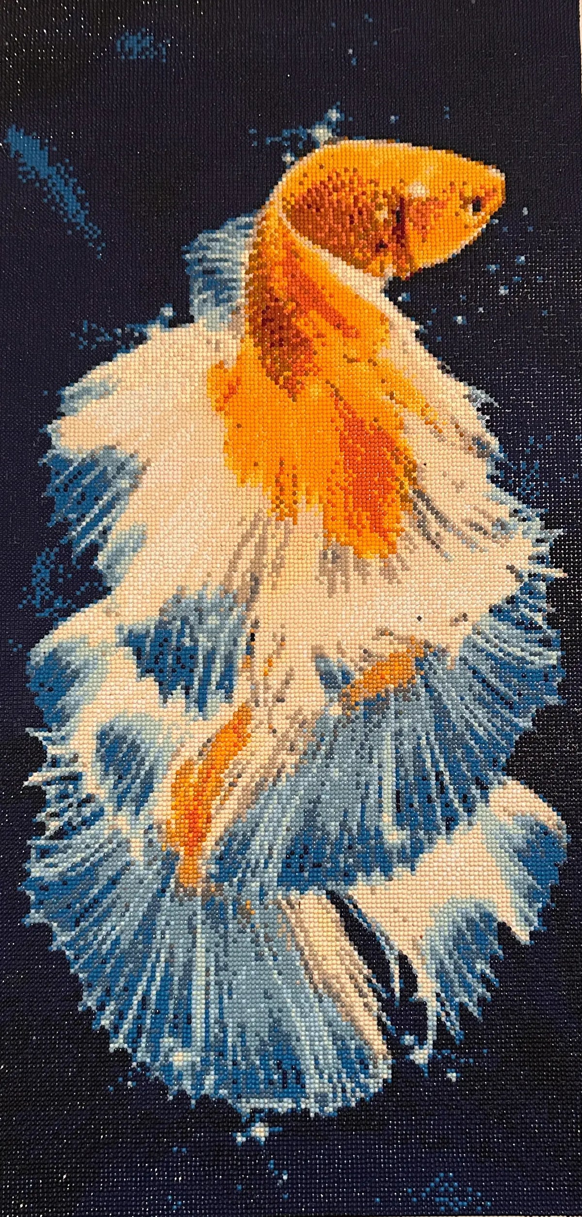 Close-up diamond painting of an orange-gold betta with ruffled white and blue fins against a dark navy background