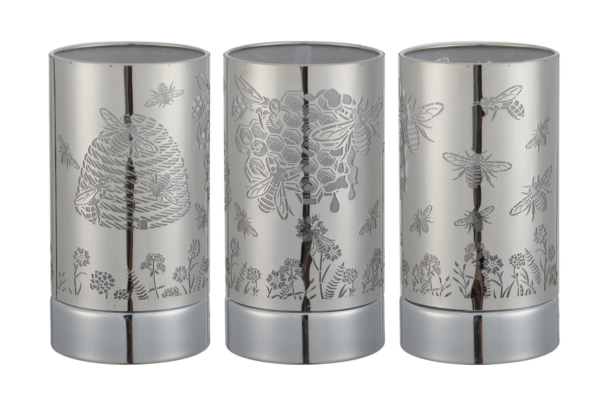 Three cylindrical silver metal wax warmers shown side-by-side with laser-cut honeybee, hive, honeycomb and floral patterns.
