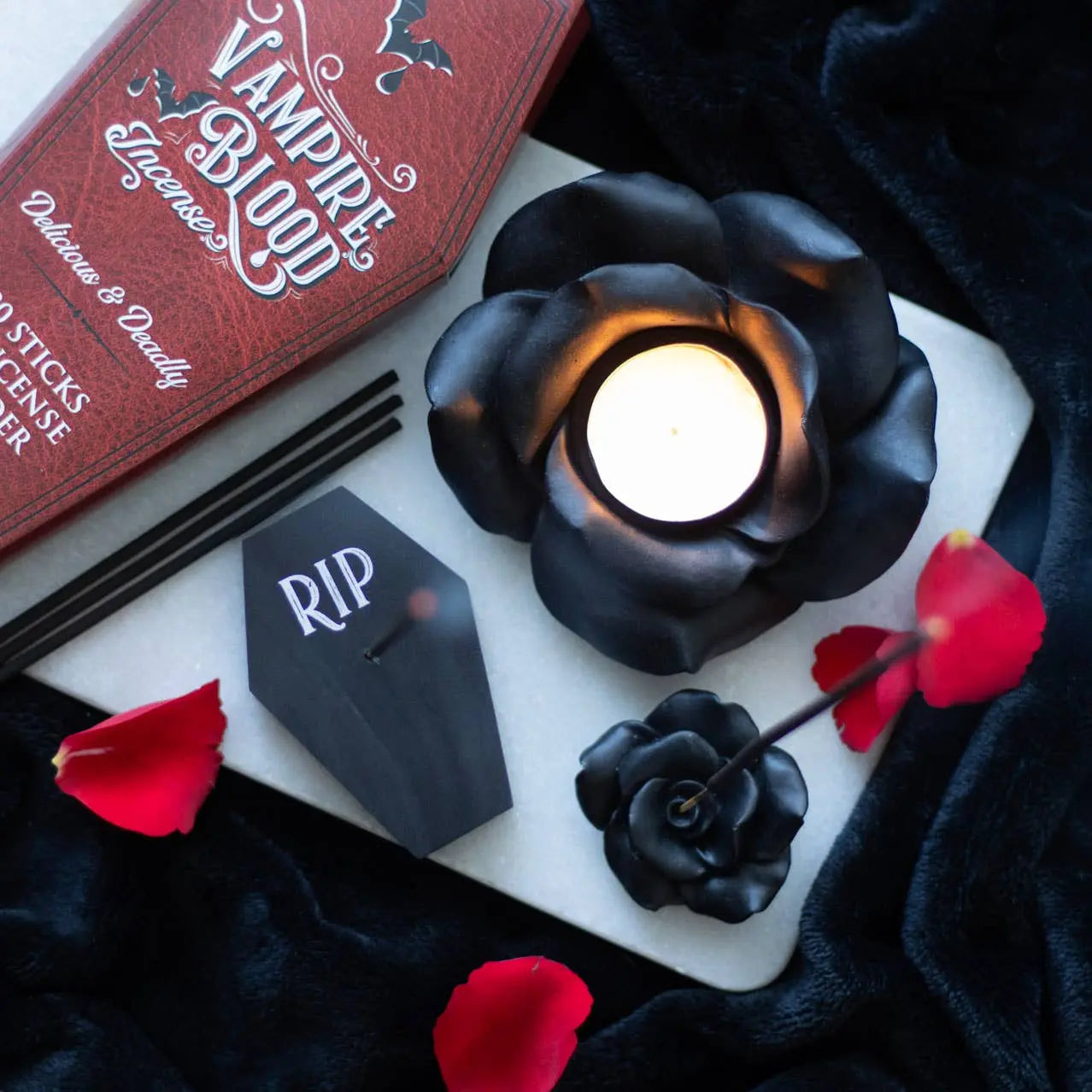 Black rose tealight candle holder with lit tealight, surrounded by rose petals and vampire-themed incense.