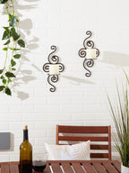 Scrollwork candle sconces mounted on a white brick wall, adding ambiance to a cozy outdoor dining area.