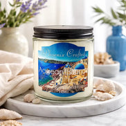 Aegean Islands Candle in a glass jar with coastal scenery label, surrounded by seashells and decorative elements.