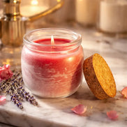 Alluring Berry Candle in a glass jar with cork lid, resting on a marble surface with flowers and lavender.