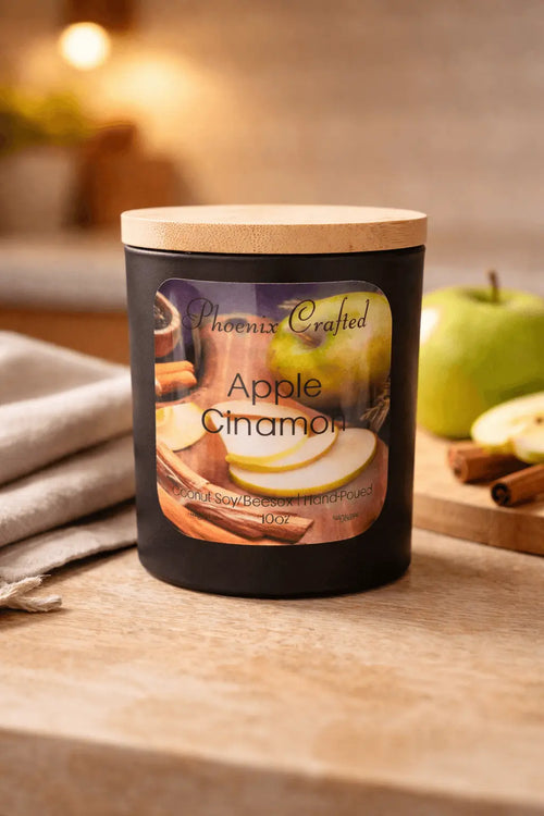 Apple Cinnamon candle in a black jar with wooden lid, styled with sliced green apple and cinnamon sticks on a wooden surface, all‑natural hand‑poured candle by Phoenix Crafted