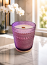 Cream wax candle with a single wooden wick in a purple hobnail glass vessel on a round wooden coaster.