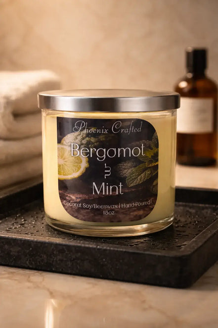 Phoenix Crafted Bergamot & Mint candle — pale yellow wax in clear glass jar with silver lid and black label, set on a wet black tray.
