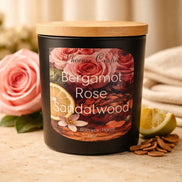 Bergamot Rose & Sandalwood Candle in a black container with a wooden lid, surrounded by fresh roses and lemon.
