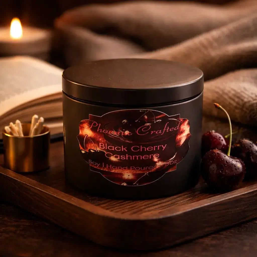 Black Cherry Cashmere Candle in a black jar on a wooden tray with cherries, book, and cozy fabric.