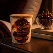 Black Cherry Cashmere Candle displayed on a nightstand with cherries and cozy decor.