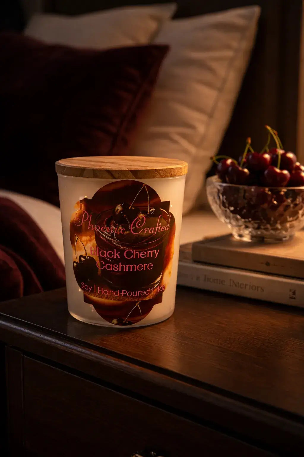Black Cherry Cashmere Candle displayed on a nightstand with cherries and cozy decor.