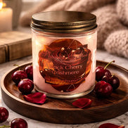 Black Cherry Cashmere Candle in a glass jar on a wooden tray with cherries and rose petals, perfect for cozy atmospheres.