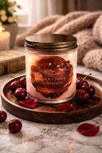 Black Cherry Cashmere Candle in a glass jar on a wooden tray with cherries and rose petals, perfect for cozy atmospheres.