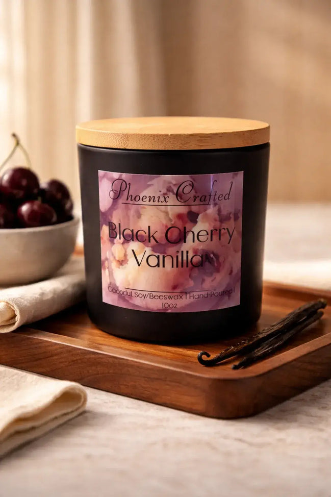 Matte black jar candle with light wood lid and purple floral label reading 'Phoenix Crafted Black Cherry Vanilla'.