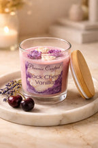 Clear jar of Black Cherry Vanilla Candle with floral design and wooden lid, surrounded by lavender and cherries.