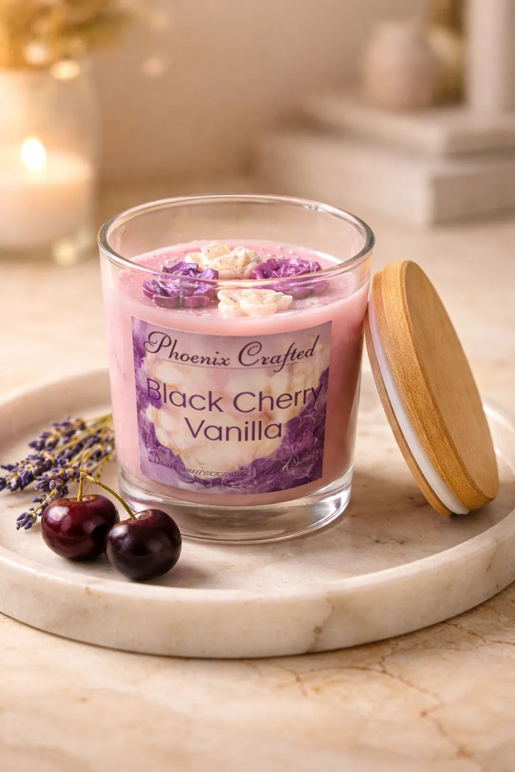 Clear jar of Black Cherry Vanilla Candle with floral design and wooden lid, surrounded by lavender and cherries.