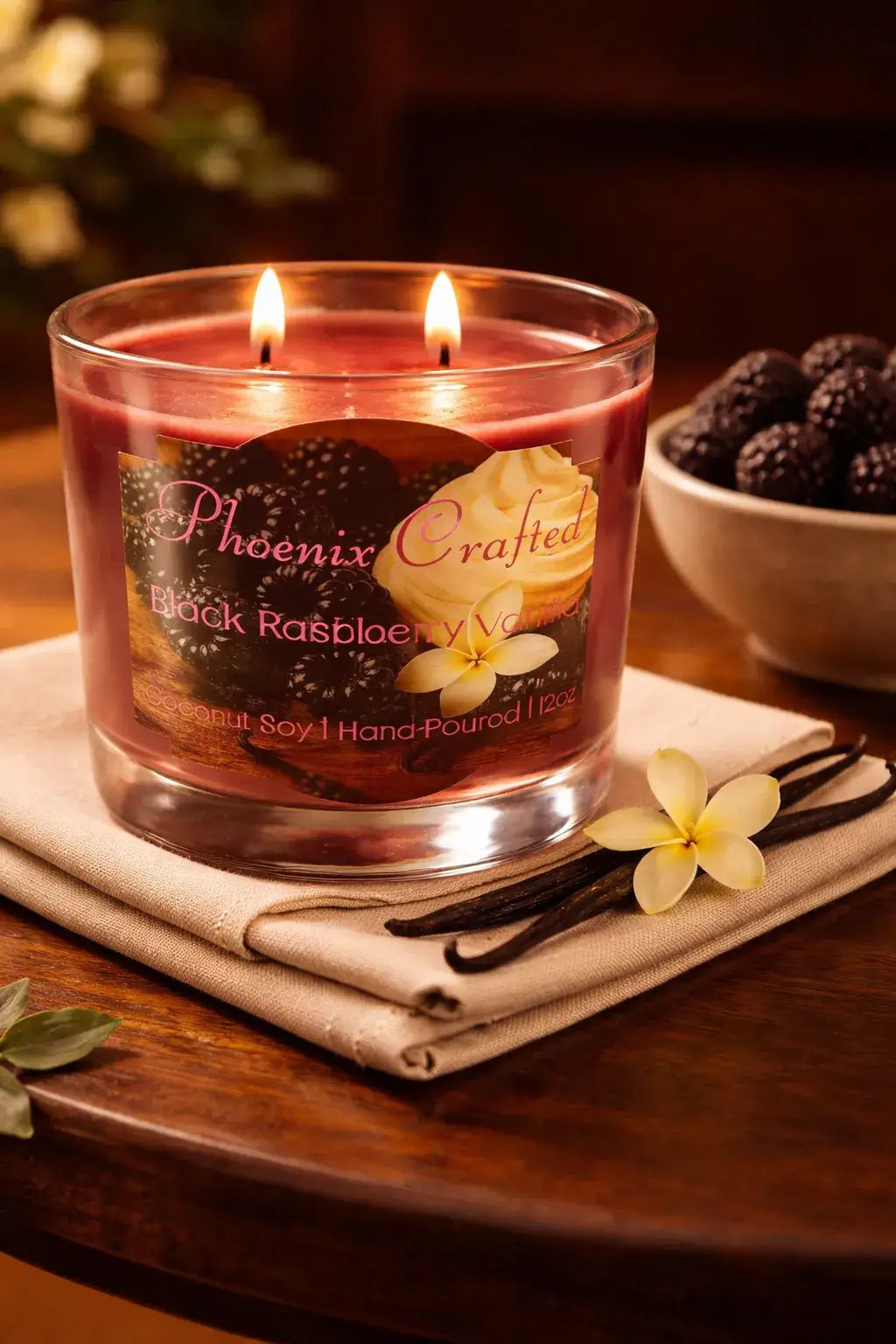Black Raspberry Vanilla Candle in a glass holder with two wicks, surrounded by blackberries and vanilla.