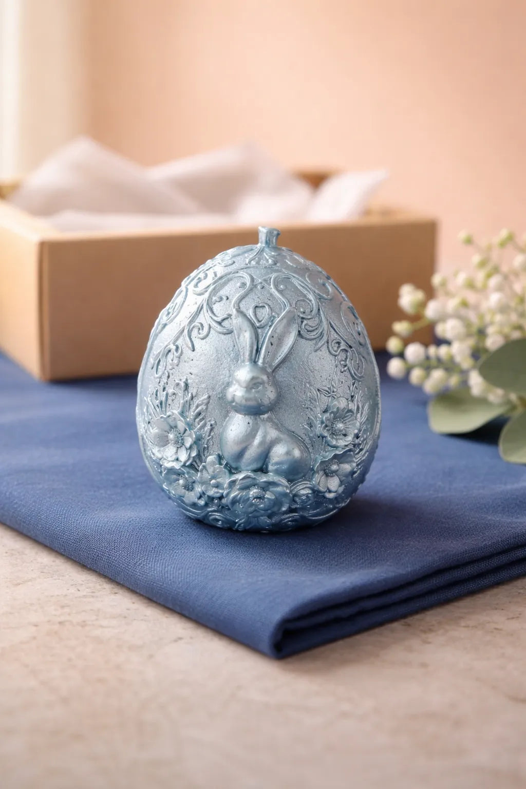 Bunny Egg Candle featuring hand-carved bunny design, soft florals, and pastel tones on a blue napkin.
