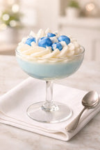 Blueberry Cream Pie Candle in a glass dish, topped with whipped cream and blue berries, on a white cloth.