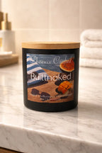 Buttnaked Candle showcased on a marble counter, featuring a wooden lid and tropical fruit accents.