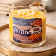 Open Butt Naked candle in a clear glass jar with yellow and white wax-flower accents on a round marble tray.