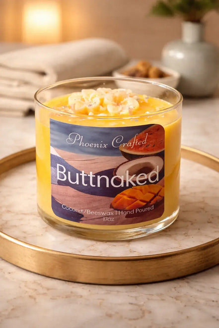Open Butt Naked candle in a clear glass jar with yellow and white wax-flower accents on a round marble tray.