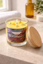 Buttnaked Candle in a glass jar with a wooden lid on a stone countertop, featuring tropical fruit scents.