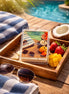 Butt Naked wax melt on a wooden tray with tropical fruits, sunglasses, and a beach towel beside a swimming pool.