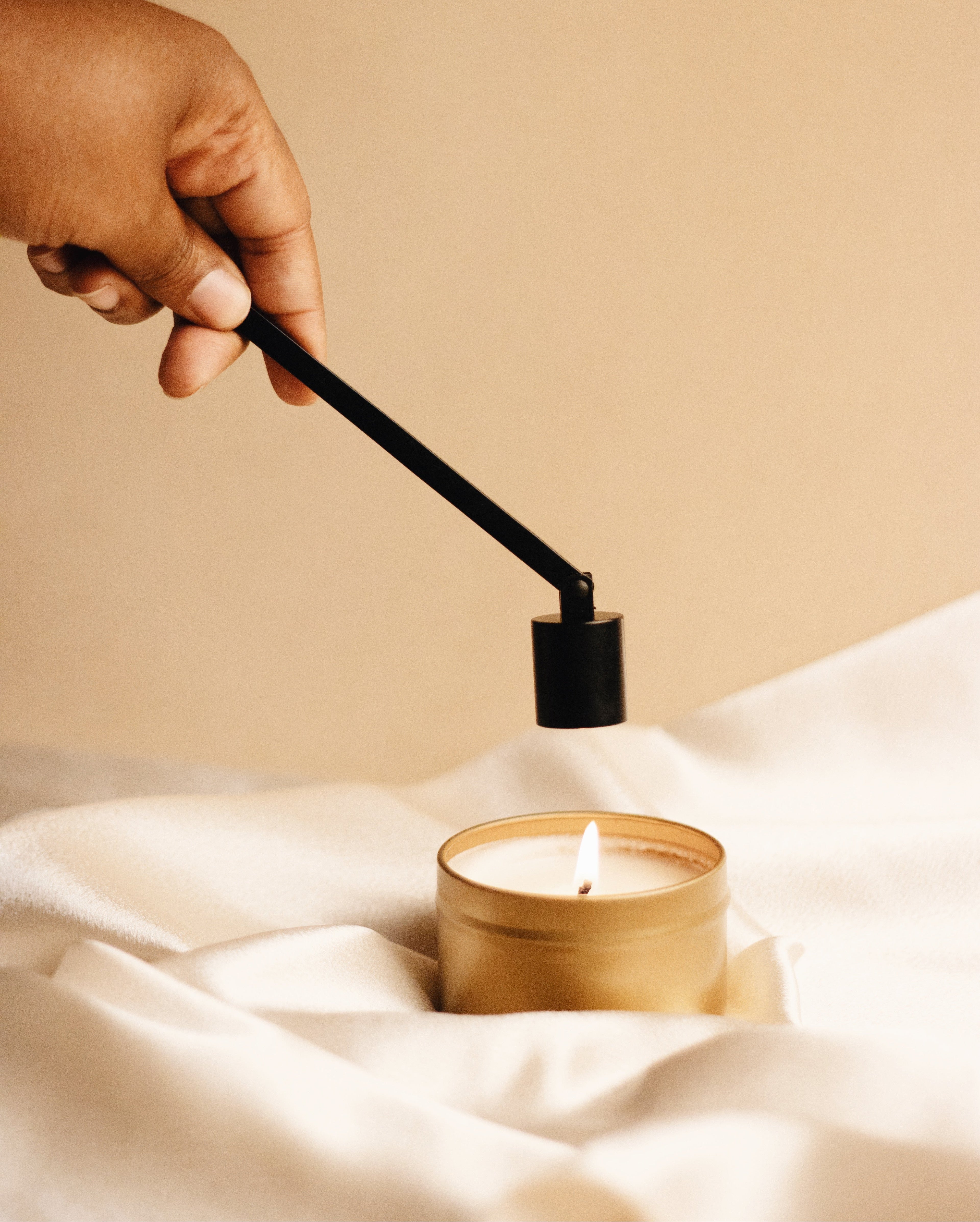 Candle care tool set with a hand using a candle snuffer on a lit candle, emphasizing proper candle maintenance.