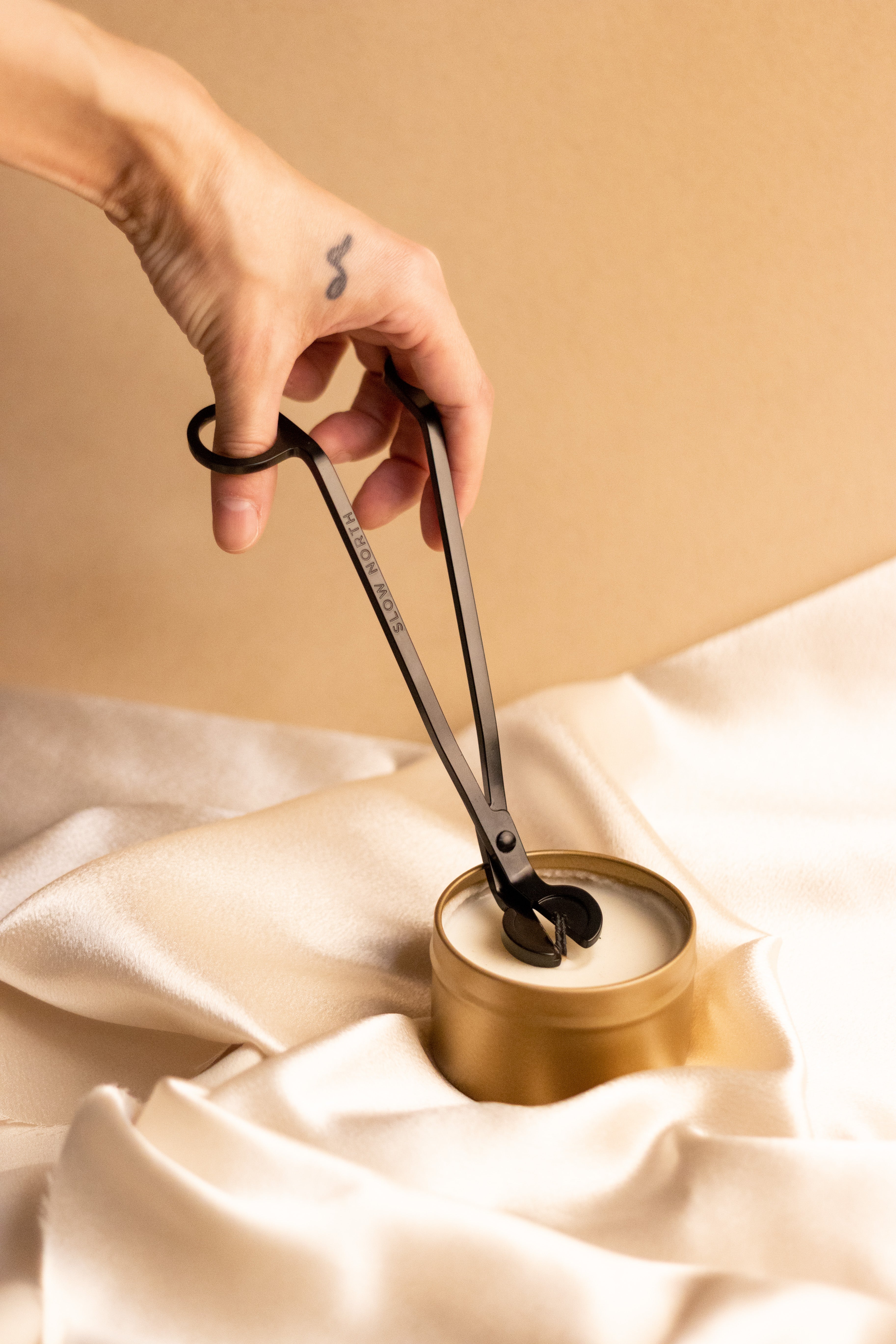 Person using the wick trimmer from a candle care tool set on a gold candle.
