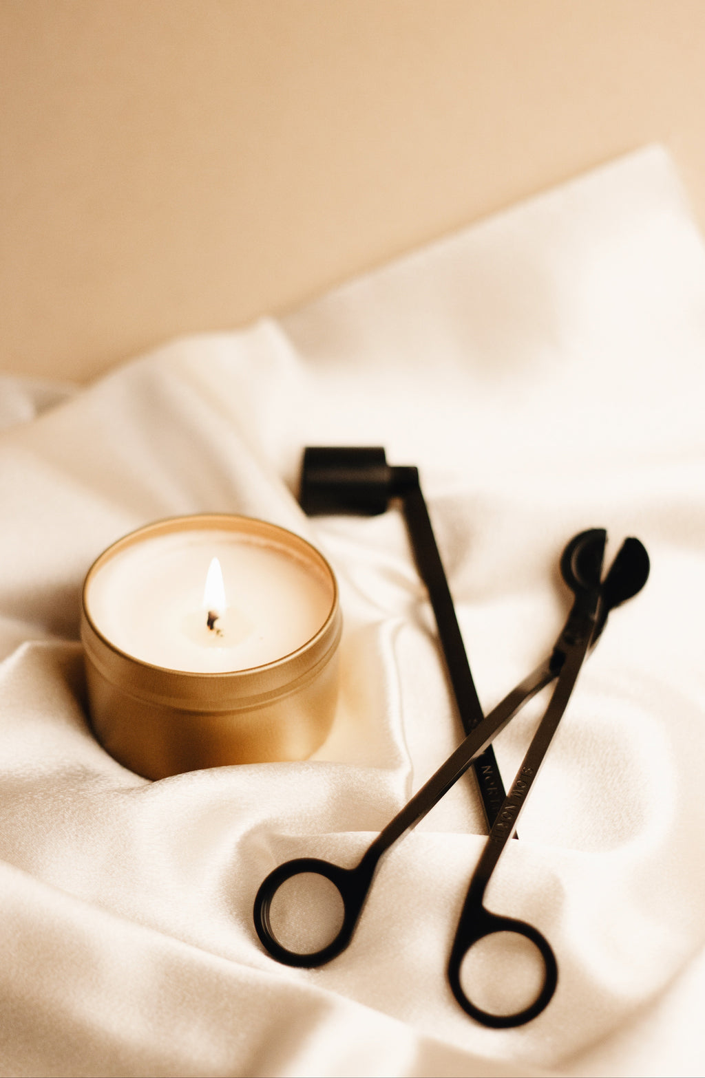 Candle care tool set featuring a candle with wick trimmer and snuffer on soft fabric.