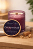Textured purple glass candle with cream wax and visible wood wick, wooden lid propped showing the readable 'Cedarwood' label.