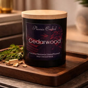 Black glass Cedarwood candle with a pale wooden lid on a rectangular wood tray with wood chips and greenery.