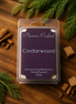 Cedarwood wax melts in a clear clamshell with a purple label, styled with cedar chips and evergreen sprigs.