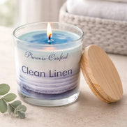 Clean Linen Candle in glass jar with wooden lid on a countertop, surrounded by soft towels and eucalyptus.