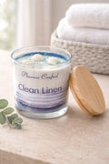Clean Linen Candle in glass jar with wooden lid on a countertop, surrounded by soft towels and eucalyptus.