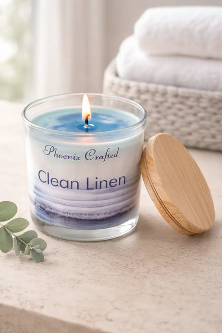 Clean Linen Candle in glass jar with wooden lid on a countertop, surrounded by soft towels and eucalyptus.