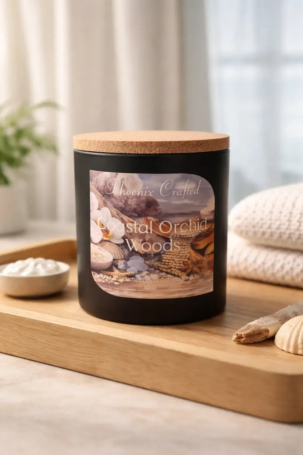 Coastal Orchid Woods Candle displayed on a wooden tray with seashells and a soft towel in a serene setting.